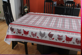Chickens (a central pattern of white, red, and grey plaid, with a border on either side of the width of a thick red line, red and grey plaid, a white field with solid red and grey chickens and red and grey plaid chickens Then another solid band of red and a band of red and grey up to the edge) opaque vinyl draped over a dining room table with matching chairs around it.