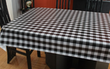 Black and White Check (black and white gingham pattern with black bands over a white background) opaque vinyl draped over a dining room table with matching chairs around it.