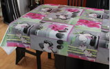 Orchids (white orchids with green leaves, dark grey smooth stones, bamboo shots and bright pink accents are arranged on grey, white and watercolour green backgrounds, arranged loosely in overlapping square motifs) opaque vinyl draped over a dining room table with matching chairs around it.