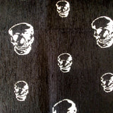 Jacquard upholstery fabric with stylized white skulls of varying sizes scattered on a black background