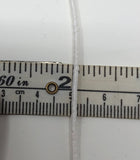 White elastic twine laid over a measuring tape, showing the twine is just over one-sixteenth of an inch (2mm) thick