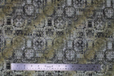 Flat swatch Du Theater fabric (neutral toned fabric with subtle circular decorative coins/medallions in white and black with grey and yellow rust coloured areas and subtle black text)
