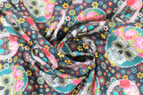 Swirled swatch Craneo fabric (black fabric with small yellow, blue, white and red flowers allover and assorted sugar skulls in white and black tossed, some wearing pink flower crowns and behind either white or teal oval frames)