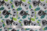 Flat swatch (side 1) Blinky fabric (white fabric with large tossed cartoon graphics wide-eyed koala bears in light and dark grey on green branches with leaves)