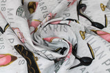Swirled swatch glam themed fabric in fashion glam (white fabric with grey fashion city names, black/pink/gold tossed high heels, assorted perfume bottles, small pink floral arrangement in vase)
