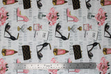 Flat swatch glam themed fabric in fashion glam (white fabric with grey fashion city names, black/pink/gold tossed high heels, assorted perfume bottles, small pink floral arrangement in vase)