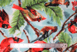 Flat swatch spruce cardinal fabric (light blue/white sky look fabric with green and brown spruce tree branches holding red cardinals, red berries, and pinecones)