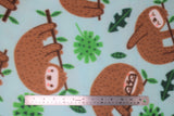 Flat swatch chillin sloths fabric (pale light blue fabric with tossed brown cartoon sloths hanging onto tree branches and green leaves throughout. Some sloths have closed eyes, some have glasses, some are smiling)