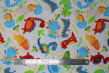 Flat swatch Baby Dinos fabric (white fabric with tossed cartoon style baby dinosaurs in various styles and colours with tossed greenery, eggs and bones all in green, blue, yellow, orange and red shades)