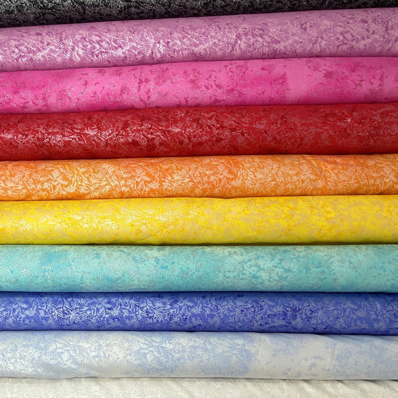 A stack of fabric bolts in a rainbow of solid shades, each covered with a shimmery silver frost pattern