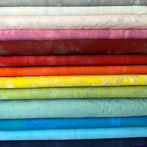 A stack of fabric bolts in a rainbow of colours, each with a faded or distressed grunge pattern.