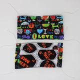 Front and back view of mask with white elastic ear loops (black mask with "I love my cat" text in various fonts and letters, cartoon cat graphics and hearts all in a rainbow coloured theme)