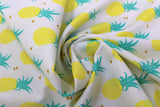 Swirled swatch of pineapple print fabric on white (tiled yellow and green pineapples with tossed tiny gold hearts)