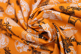 Swirled swatch of assorted Canadian custom motorcycles fabric in orange (orange fabric with tossed logo and text related to Canadian custom motorcycles "Custom" text, etc. in white, black)