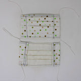 Front and back view of mask with white elastic ear loops (off white mask with medium sized spaced out polka dots in light and dark brown, white, light and dark green)