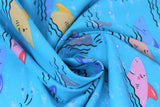 Swirled swatch sharks fabric (light blue fabric with smiling cartoon/drawing style shark heads sticking out of water in orange, pink, blue, grey, some shark fins sticking out only, black wave lines)