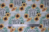 Flat swatch home sweet home fabric (white and grey subtle barn board look fabric with green leaf wreaths with yellow and black sunflowers, black cursive writing within reading "Home Sweet Home" - repeated pattern allover)