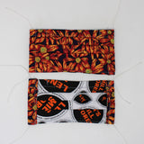 Front and back view of mask with white elastic ear loops (black mask with large orange and yellow sunflower floral collage allover)